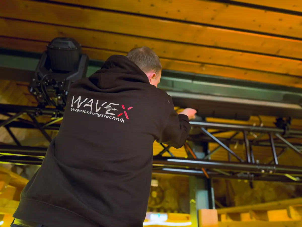 Techniker im WaveX-Hoodie richtet einen Moving Head an einer Traverse aus