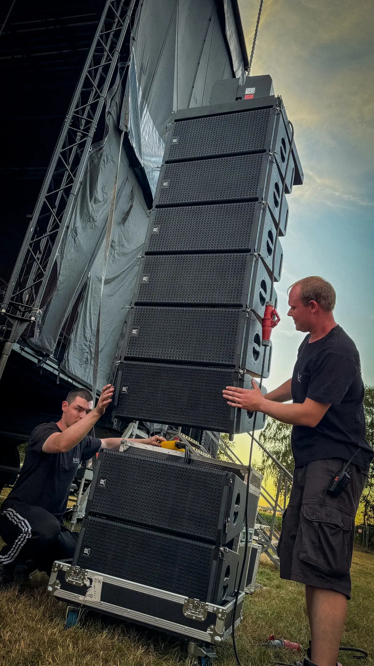 Zwei Techniker von WaveX montieren ein Line-Array an einem Bühnenturm